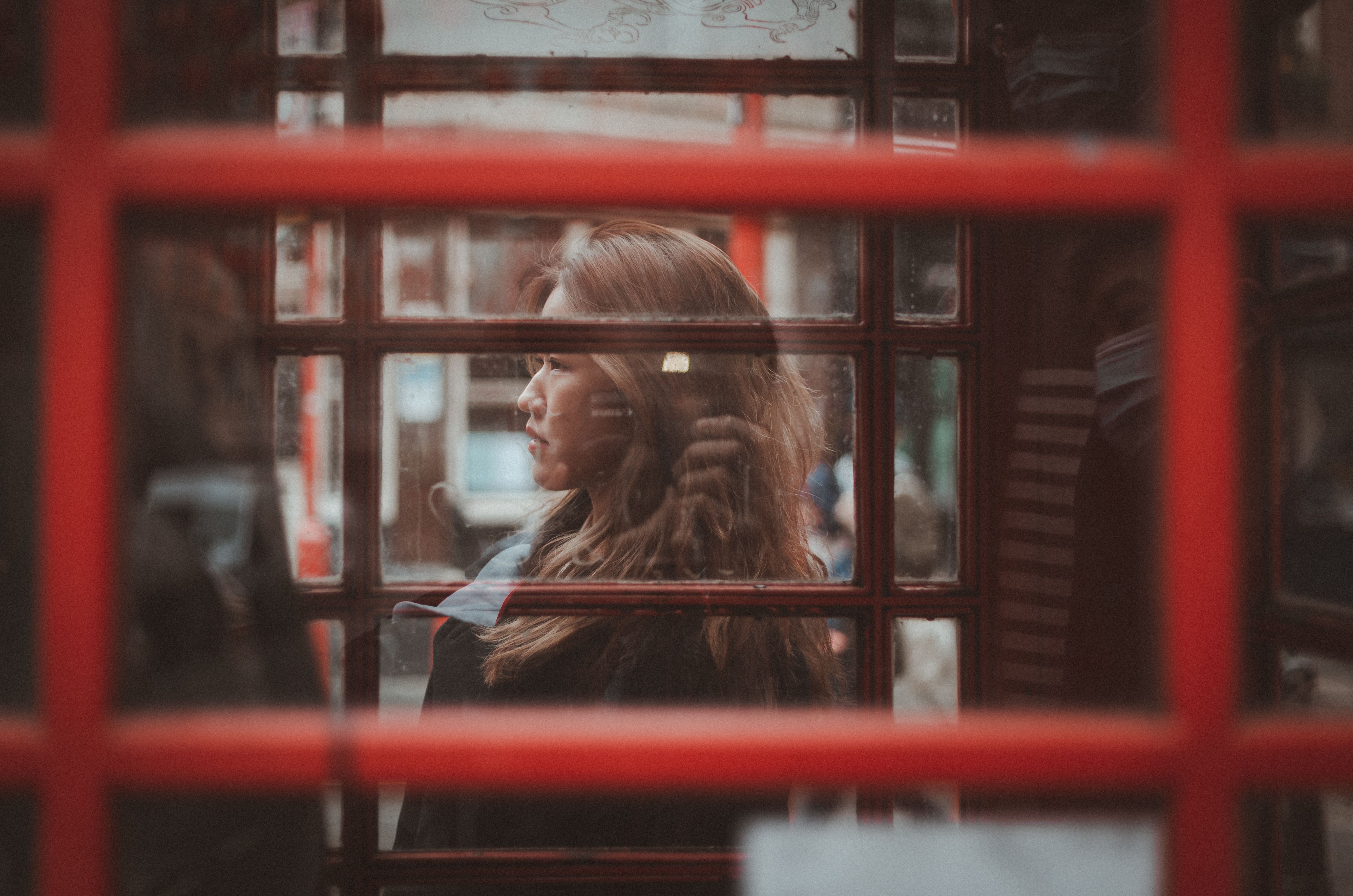 Criminal Injuries Compensation Authority Number: How to Contact CICA — A woman gazes outside from inside a classic red London phone booth, capturing urban reflections.