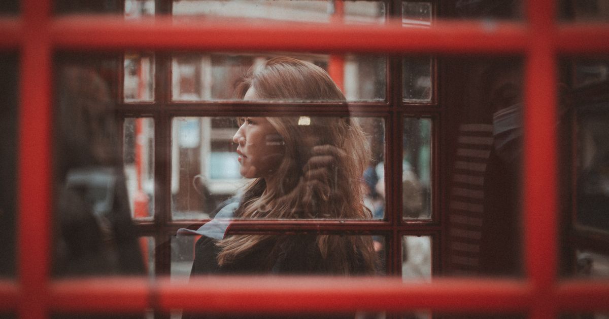 Criminal Injuries Compensation Authority Number: How to Contact CICA — A woman gazes outside from inside a classic red London phone booth, capturing urban reflections.