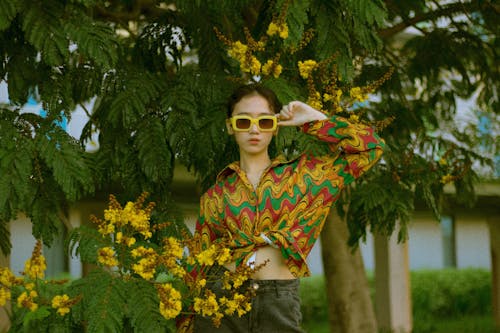 Woman Posing near Green Tree Holding her Sunglasses