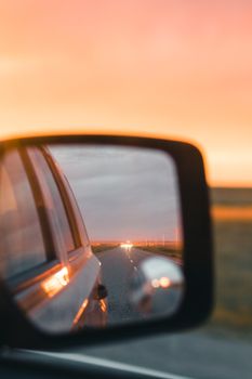 Reflection of a scenic sunset view on the road through a car's side mirror.