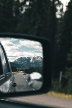 A scenic mountain landscape reflected in a car's side mirror during a road trip.