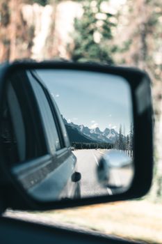 Reflection of a mountain landscape in a car side mirror during a road trip.