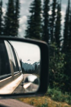 Reflection of a mountainous landscape seen through a car's side mirror during a road trip.