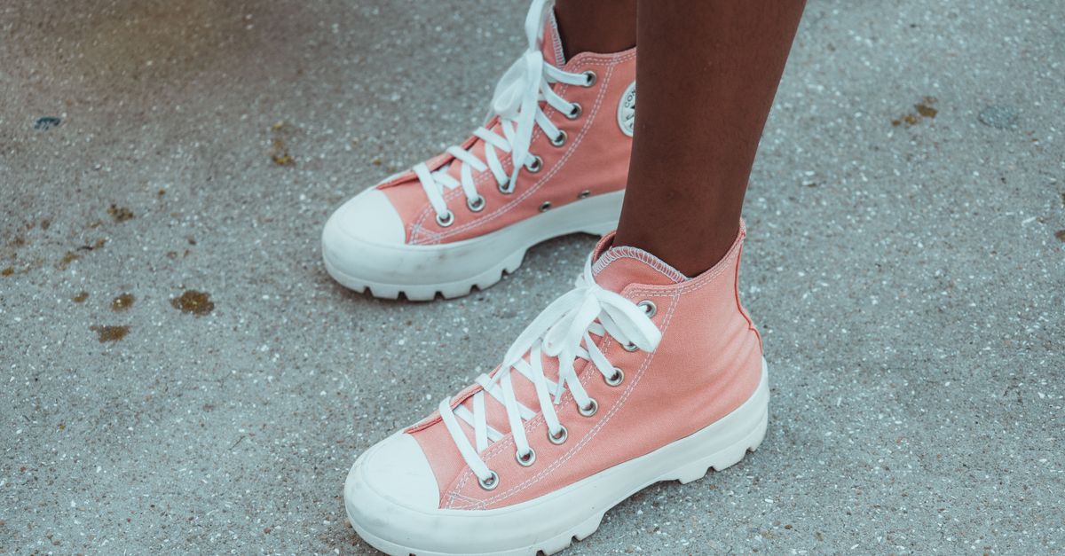 Close-up of pink canvas high-top sneakers on a textured pavement surface.