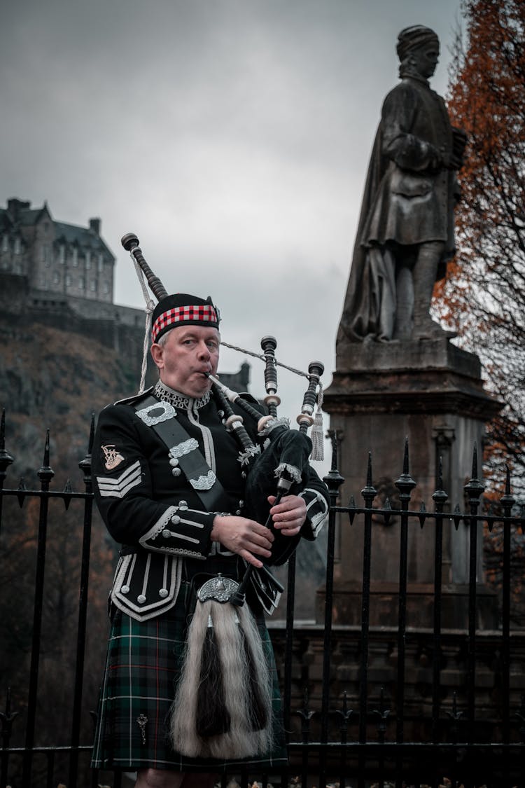 Man In Traditional Costume Playing On Bagpipe Outdoors