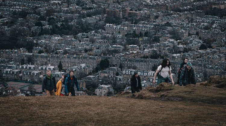 People Climbing A Hill And Cityscape In Background