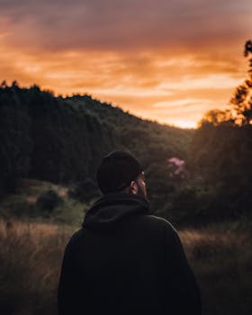 A man in a black cap admires a stunning sunset over a forest landscape in Brazil.