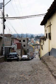 Picturesque cobblestone street in a colorful urban town under a cloudy sky.