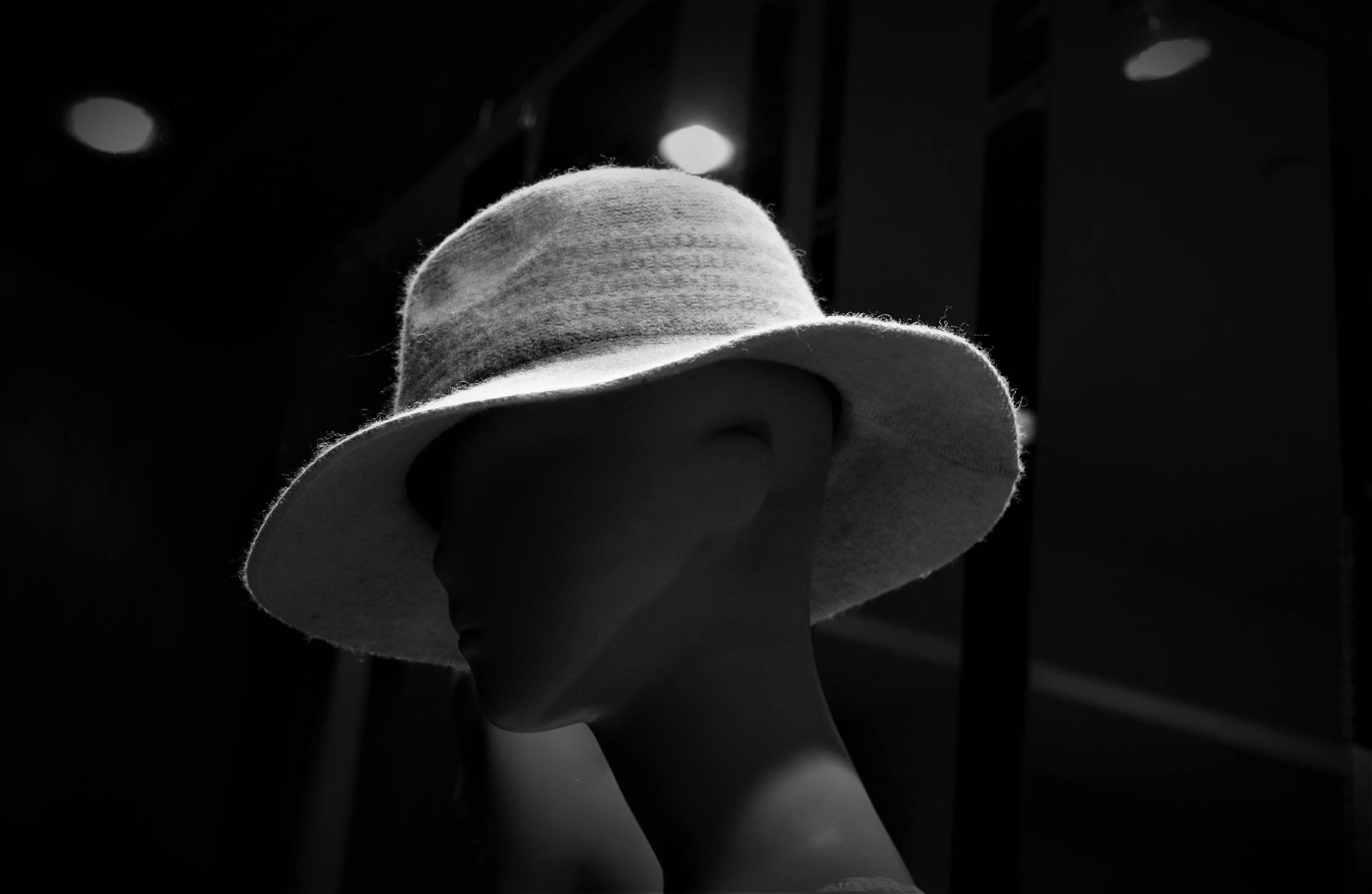 Dramatic black and white portrait of a mannequin wearing a fashionable white hat in moody lighting.