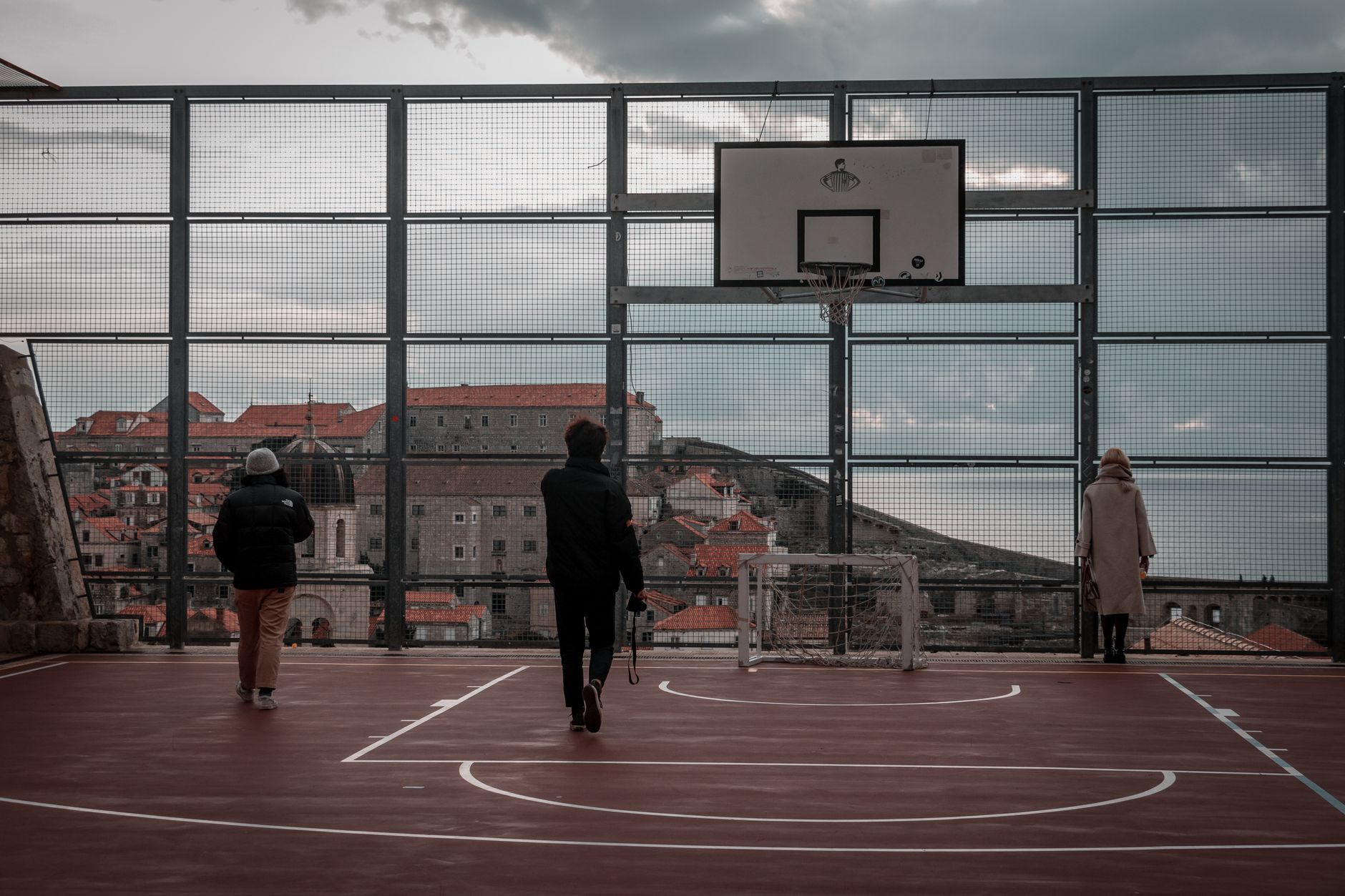 Stylish individuals on a rooftop basketball court with Dubrovnik's historic skyline in the background.