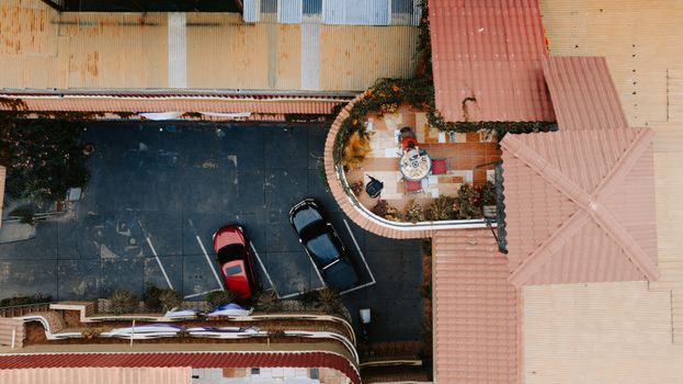 Aerial photograph of a courtyard with parked cars and a tiled terrace decorated with plants.