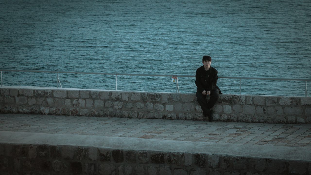 a solitary man in black clothes sits on a seawall overlooking the adri
