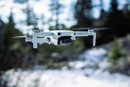 A close-up of a mini drone flying over a winter landscape in a forest setting.