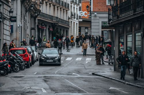 Free Vibrant street view in Madrid with people walking and cars parked, capturing city life. Stock Photo