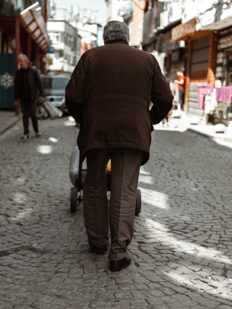 Man In Brown Jacket Pushing A Hand Truck