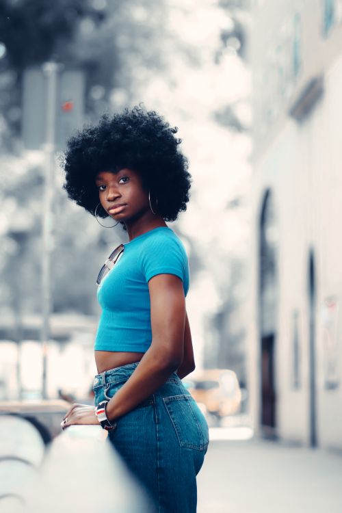 Free Young black woman with afro hairstyle in urban setting, wearing blue crop top and jeans. Stock Photo