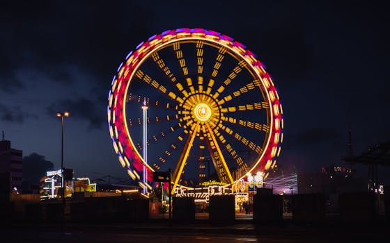 Illuminated Ferris wheel spinning against a night sky, creating vibrant trails in an urban carnival scene.