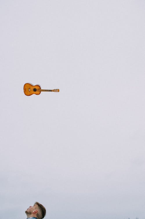 Free Man Looking Up at a Brown Wooden Guitar Stock Photo