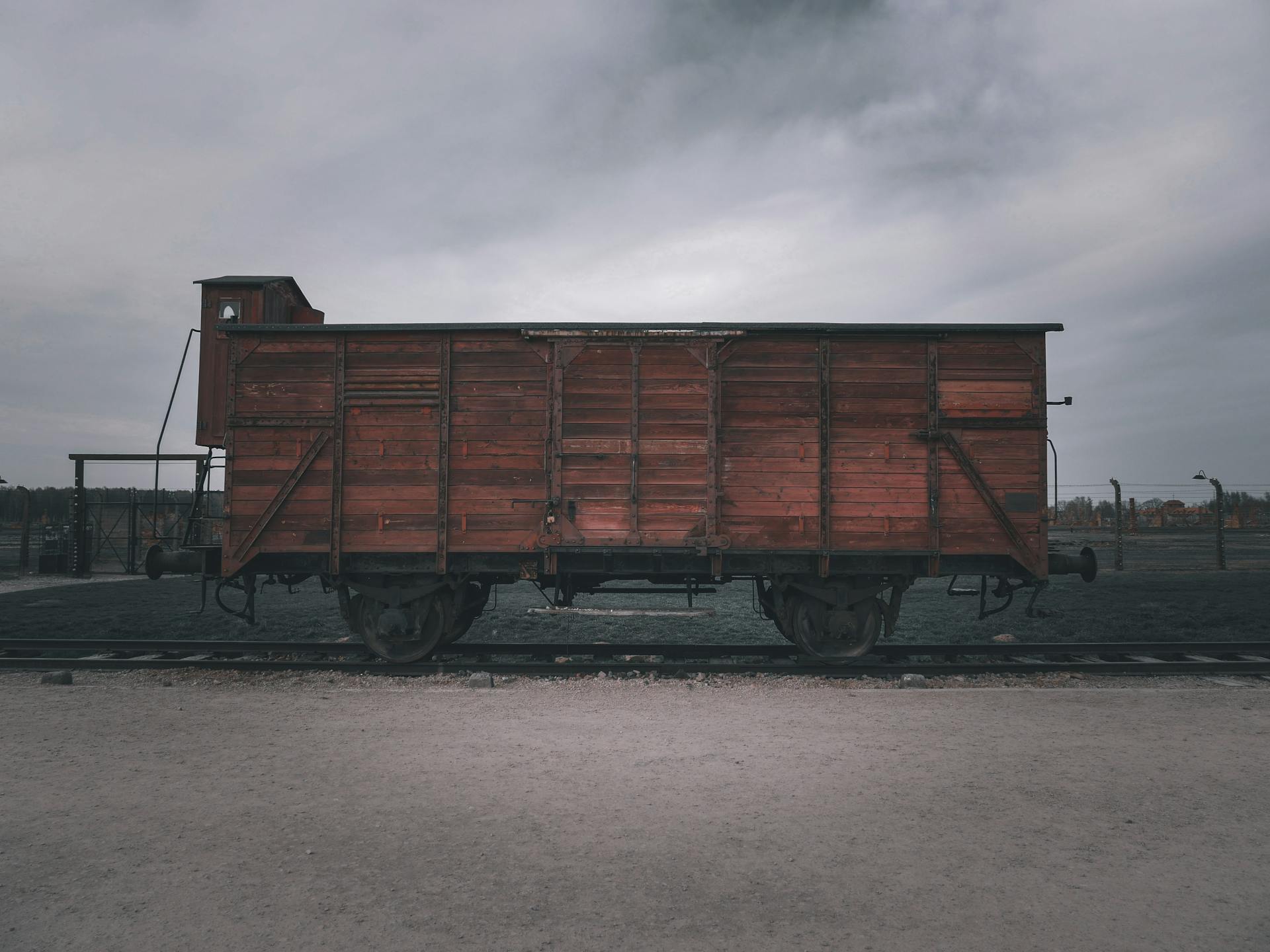 Old wooden train cargo car on railway track under cloudy sky.