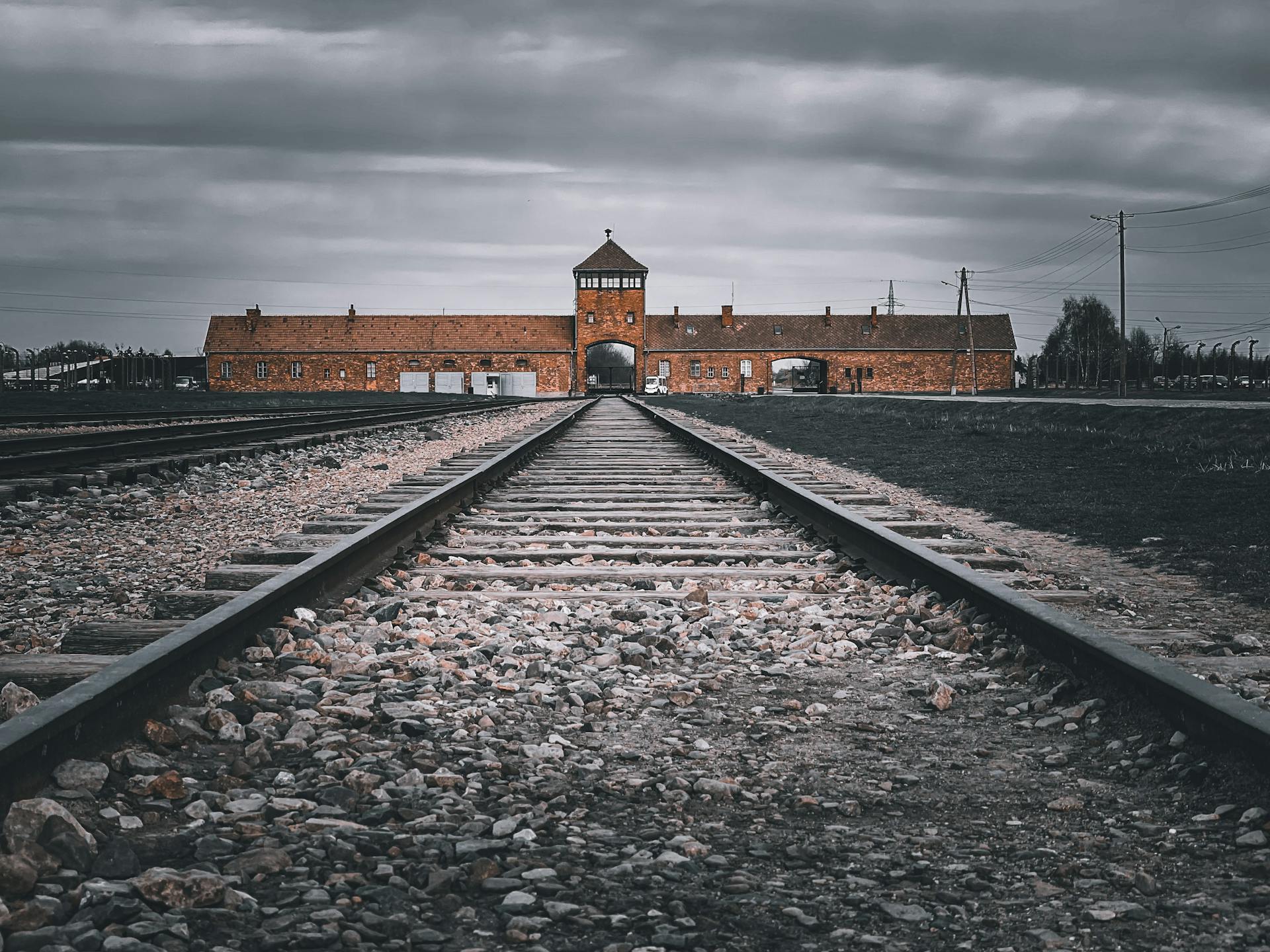 Dramatic perspective of railroad tracks leading to a historic brick building under gray skies.