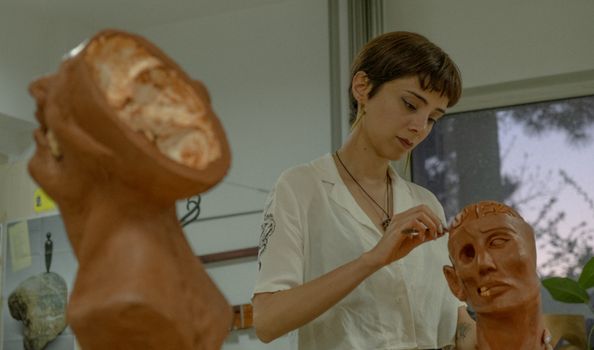 A woman artist carefully sculpting a clay model of a human head indoors.