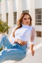 Woman in White Crew Neck T-shirt and Blue Denim Jeans Sitting on White Wooden Bench