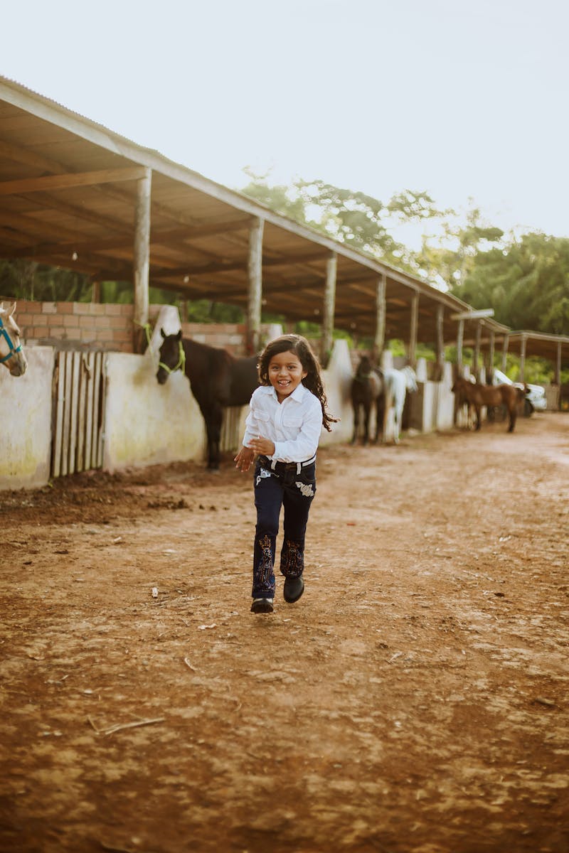 Little Girl Running Past Stables with Horses