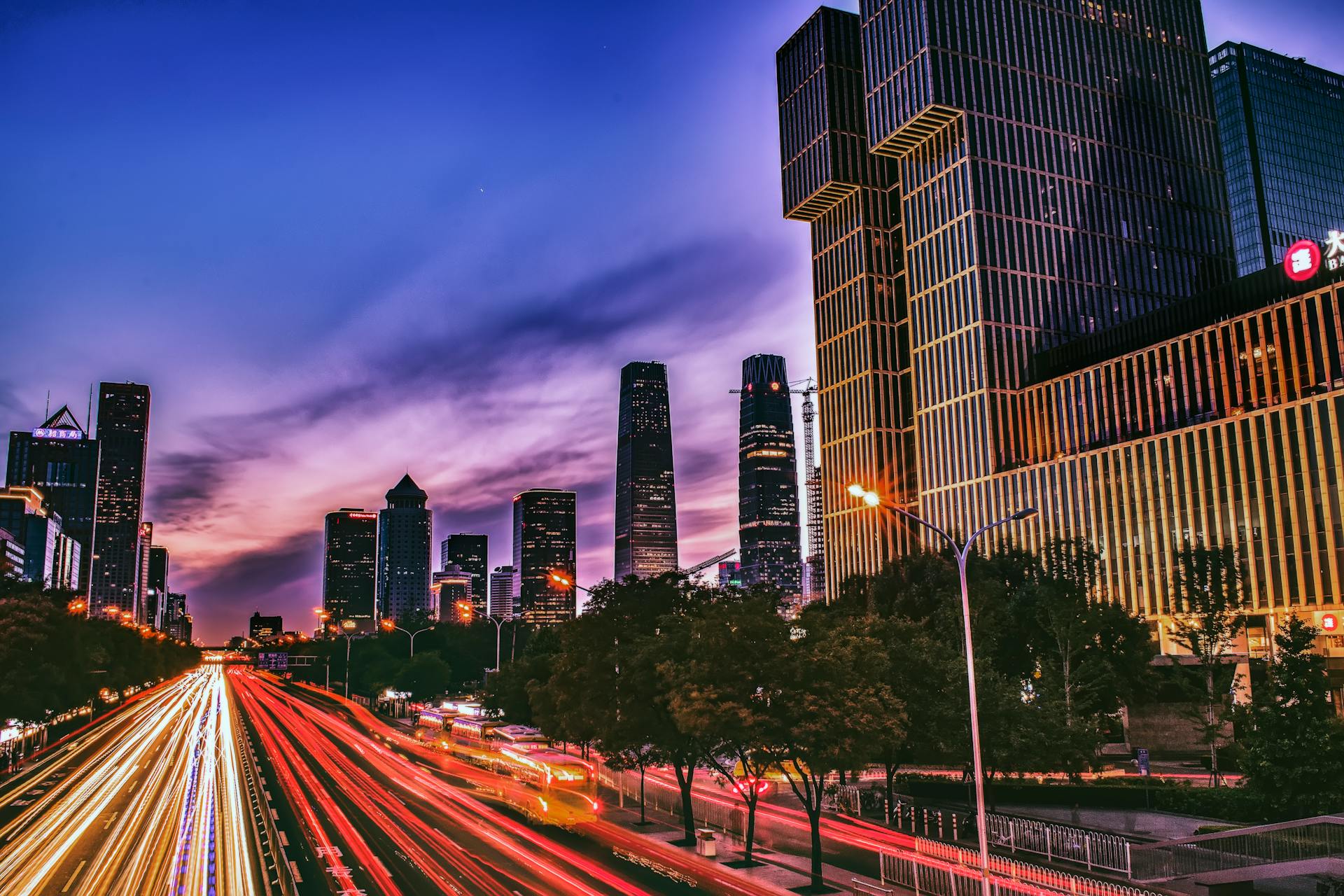 Dramatic Beijing skyline at twilight with spectacular light trails on busy highway, creating a vibrant urban scene.