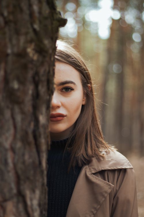 Free A mysterious portrait of a woman behind a tree, capturing an enigmatic forest vibe. Stock Photo