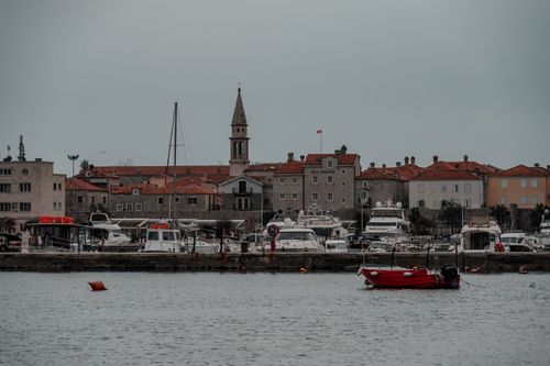 Free Picturesque view of Budva's historic waterfront with boats and the iconic bell tower under a cloudy sky. Stock Photo