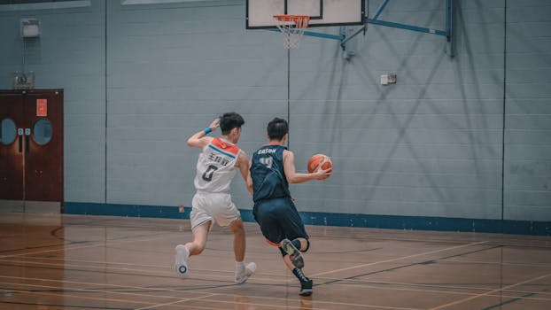 Two men playing basketball in an indoor court, showcasing athletic motion and competition.