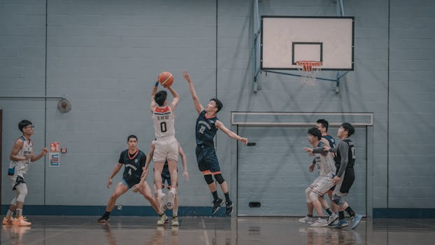 A dynamic indoor basketball game scene featuring players in action with a jump shot attempt.