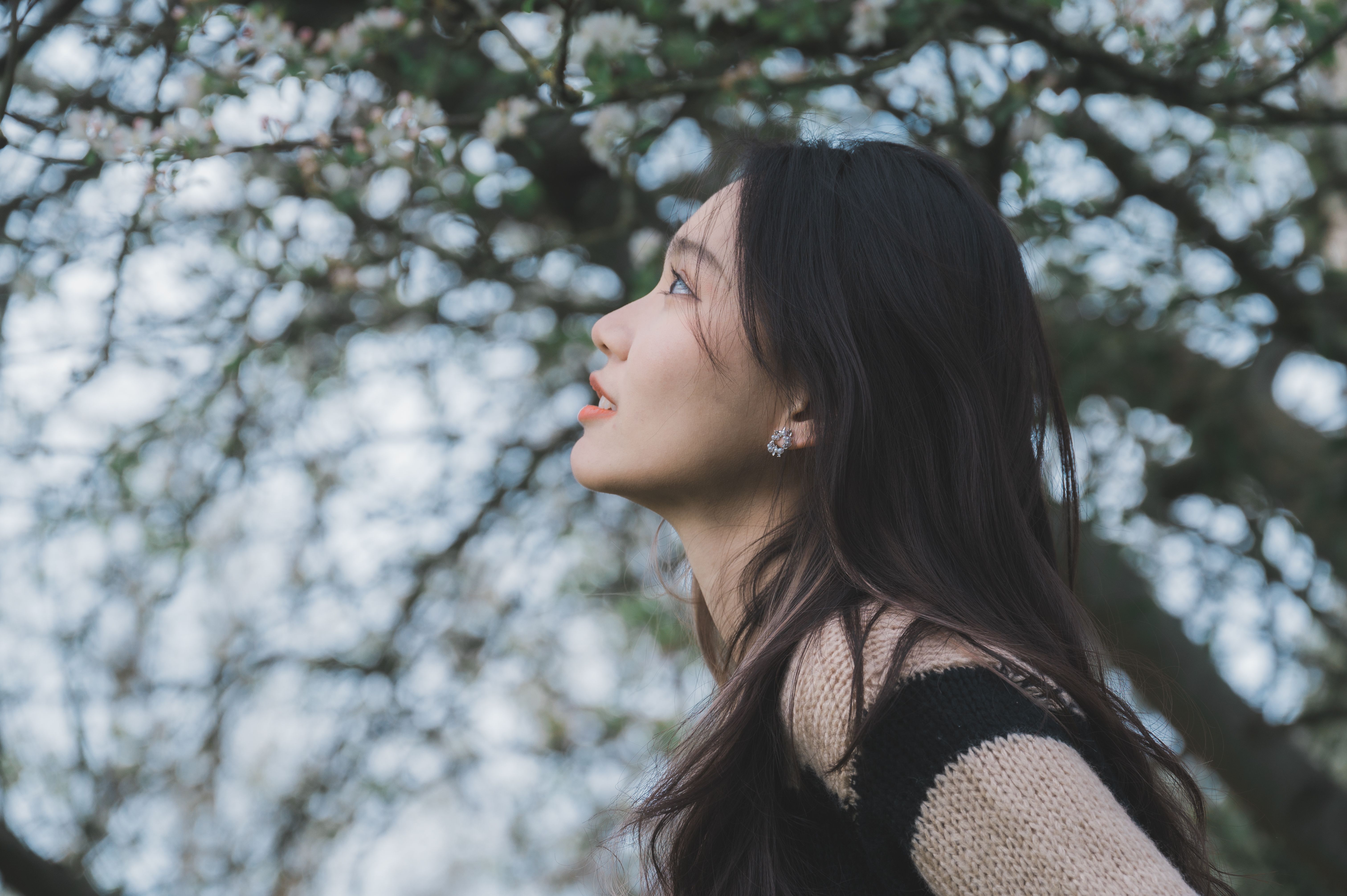 Serene woman enjoying the beauty of nature surrounded by blossoming trees in a tranquil setting.