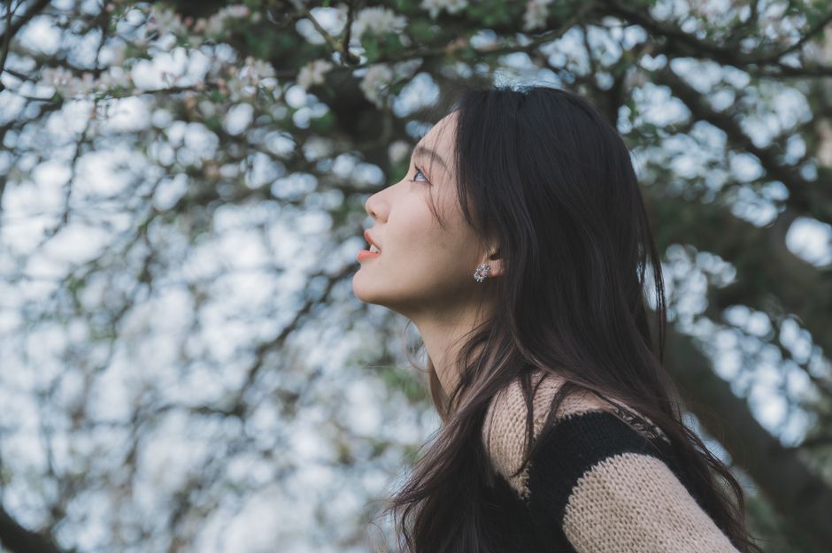 Serene woman enjoying the beauty of nature surrounded by blossoming trees in a tranquil setting.
