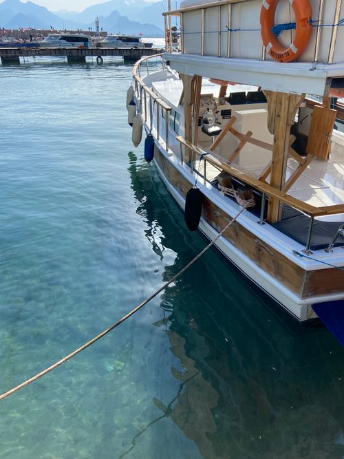 Free A rustic wooden boat docked at a serene marina with clear blue waters and scenic mountain background. Stock Photo