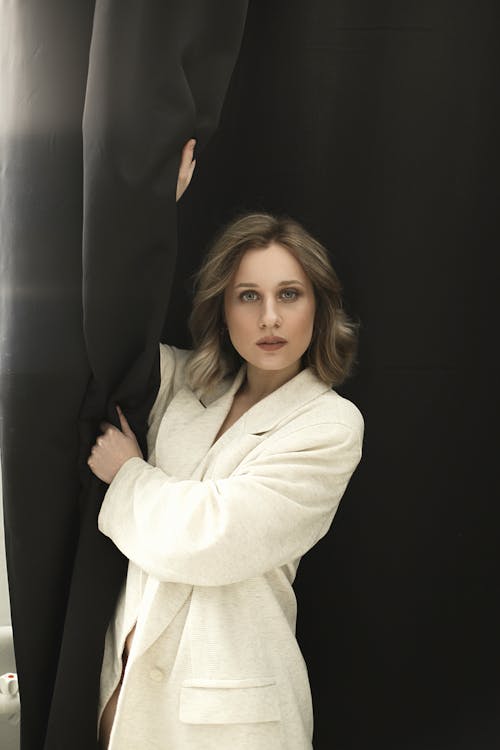 Free A Woman in White Coat Standing Beside Black Curtain Stock Photo
