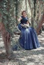一位身着惊艳蓝色礼服的女士，优雅地坐在森林场景的秋千上