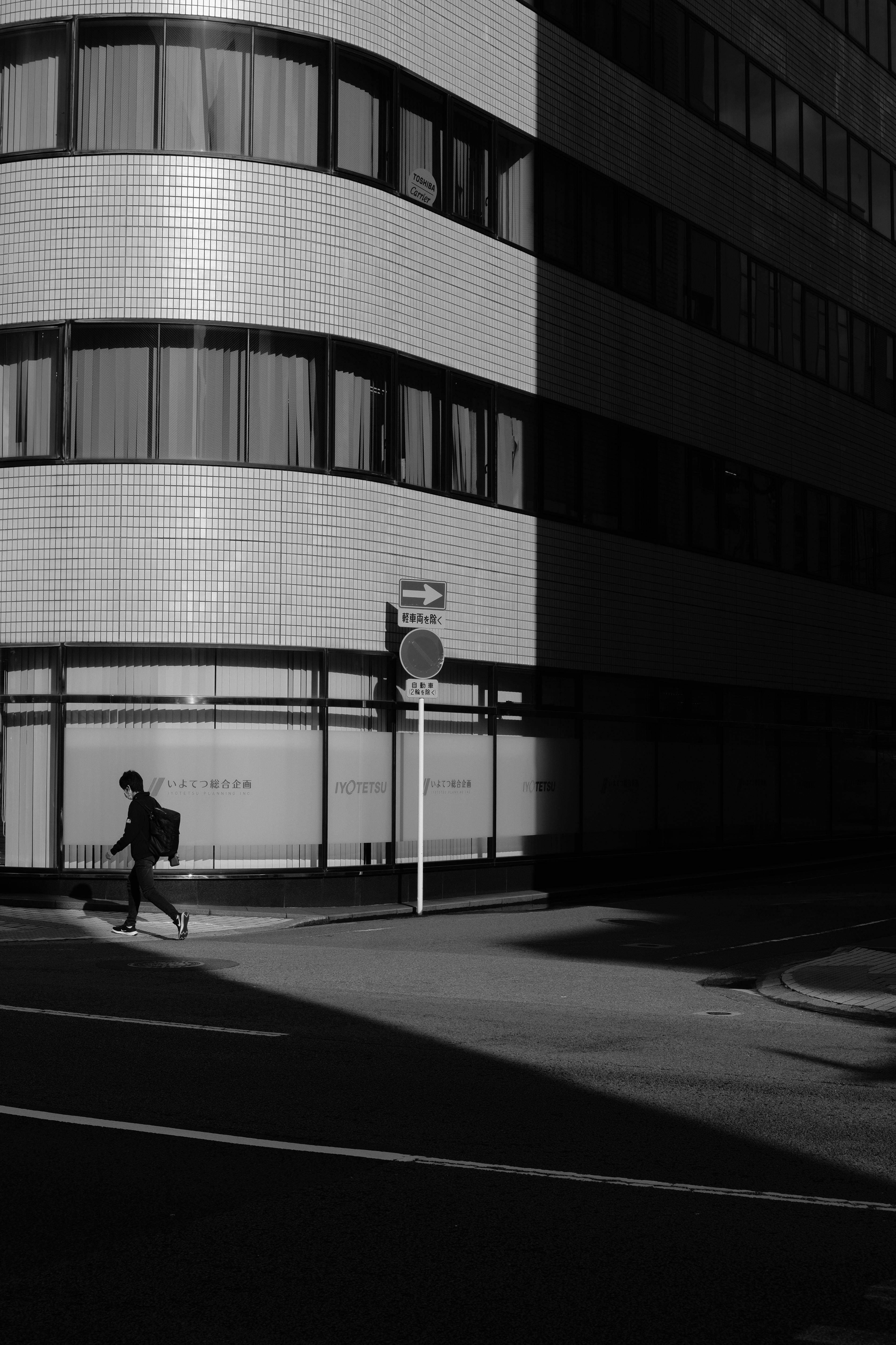 Free A person walks briskly past a modern city building in black and white. Stock Photo