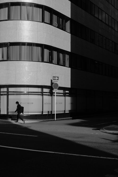 Grayscale Photo of a Man Walking by the Building