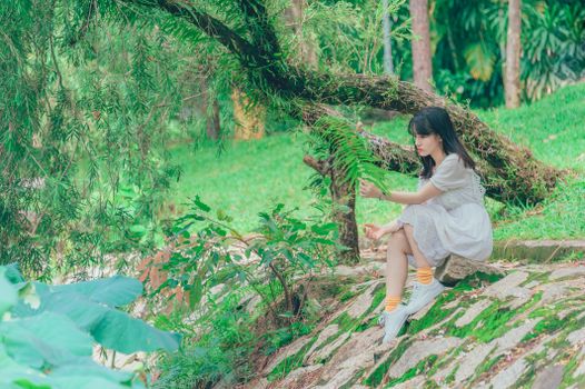 A young woman in a white dress enjoys a peaceful moment surrounded by lush greenery in a park.
