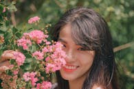 亚洲女人微笑着站在充满活力的粉红色花朵旁，突显了自然之美