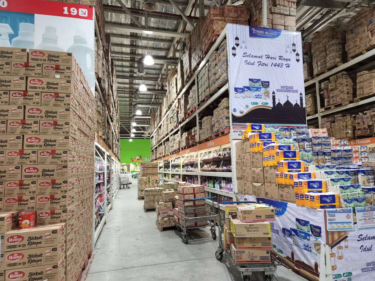 Person checking purchase history on a smartphone at a table with bulk groceries to track Costco price drops and refunds.