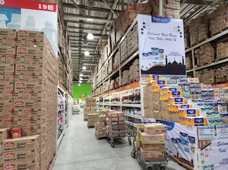 High shelves in a warehouse stocked with a variety of merchandise and large cardboard boxes.