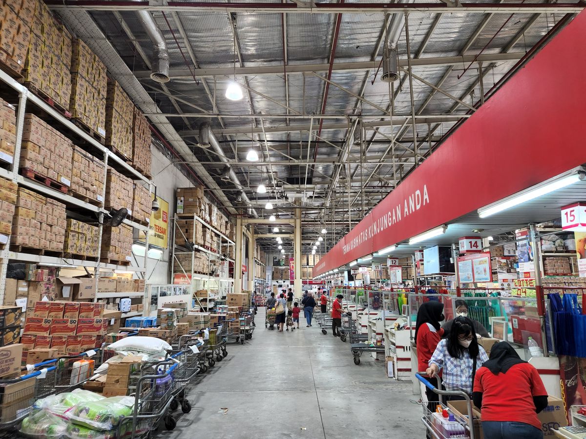 Vibrant warehouse scene showcasing rows of stocked shelves and busy shoppers with carts.