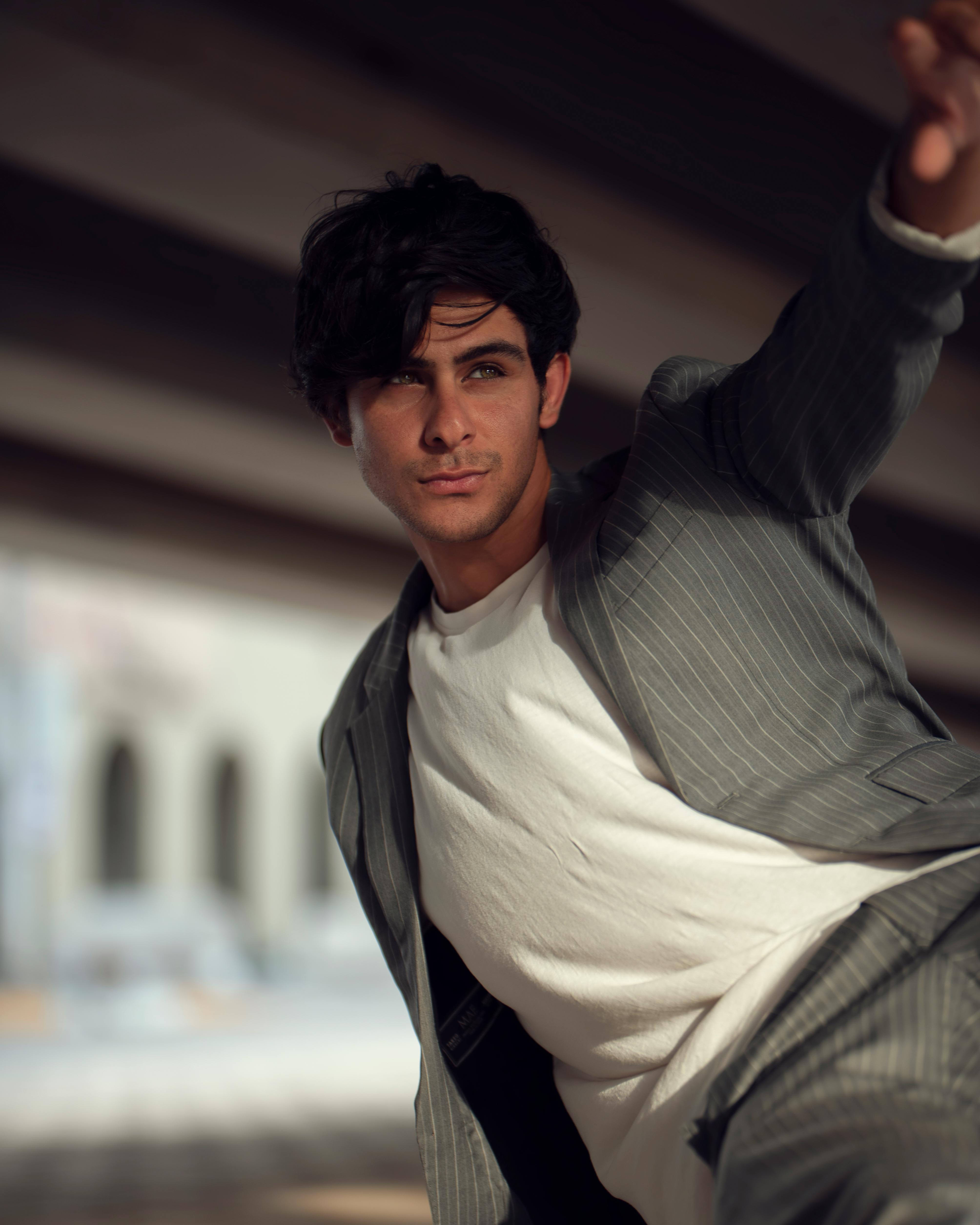 A fashionable man in a gray suit poses confidently outdoors, showcasing modern style.
