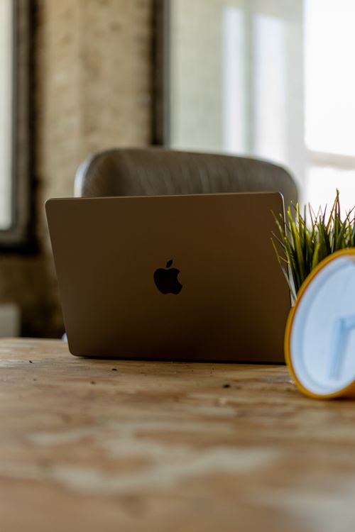 Free Modern workspace featuring a laptop, wooden desk, clock, and indoor plant for a contemporary feel. Stock Photo