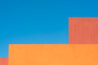 Vibrant orange and red geometric wall structures set against a bright blue sky.