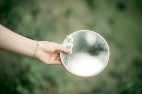 A Person Holding a Round Mirror and Angel Breaths Flower