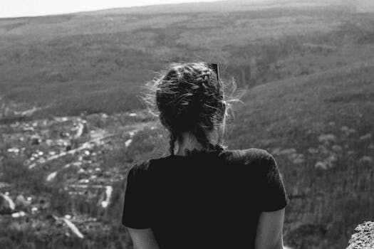 Back view of a woman enjoying a scenic mountain view in black and white.
