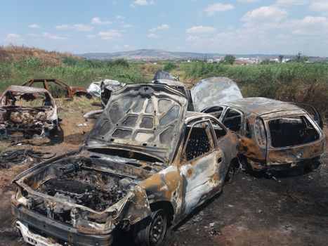 Abandoned cars rusting in an outdoor junkyard under a sunny sky.